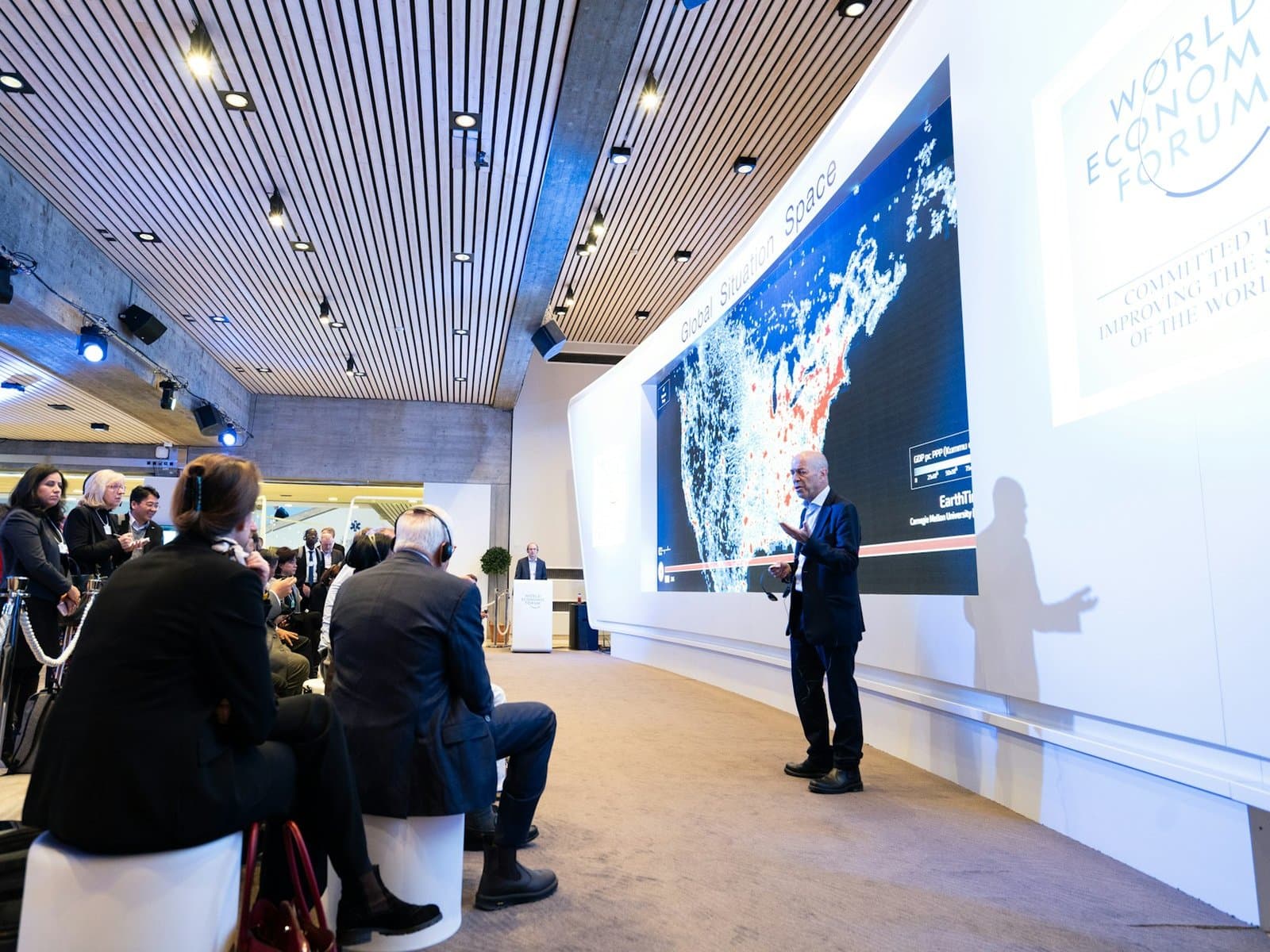 Speaker presenting to a corporate audience beside a large screen